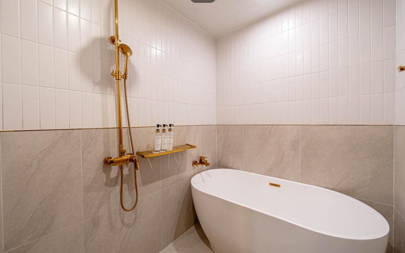 A bathroom with a freestanding bathtub, a gold showerhead, and a shelf with toiletries.