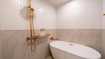 A bathroom with a freestanding bathtub, a gold showerhead, and a shelf with toiletries.