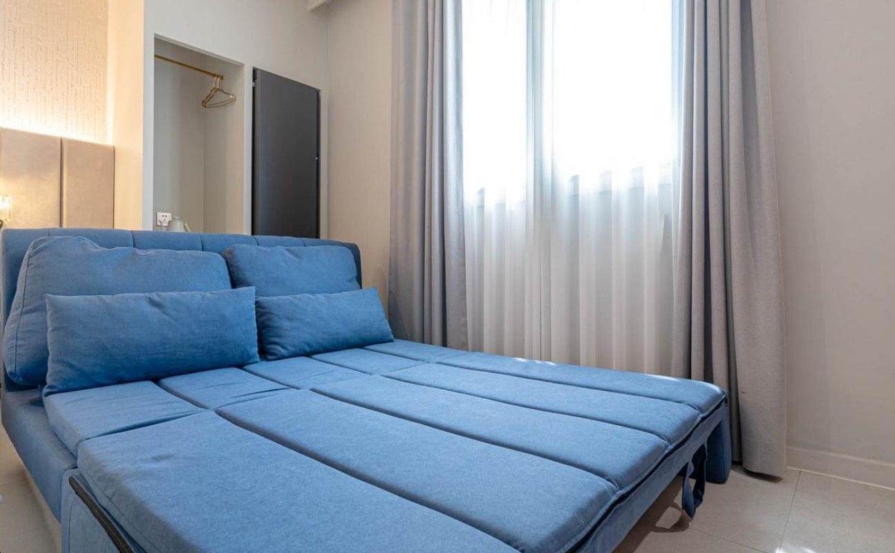 A bed with a blue mattress and pillows, a bedside table, and a window with curtains.