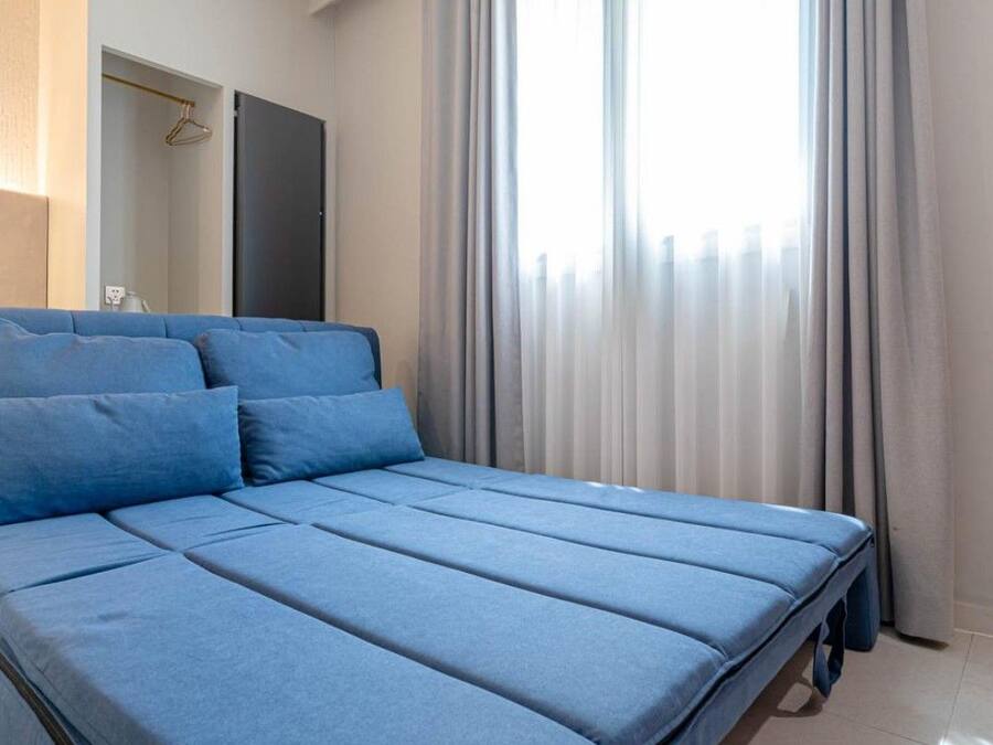 A bed with a blue mattress and pillows, a bedside table, and a window with curtains.