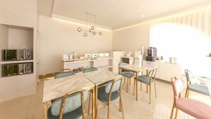 A modern dining area with a marble table and gold chairs, a kitchen area with a microwave and coffee machine, and a ceiling light fixture. - Signature Denbasta Hotel (Busan)