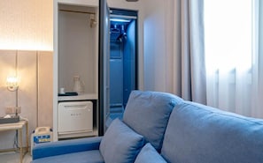A room with a blue sofa, a small table with a lamp, and a minibar.