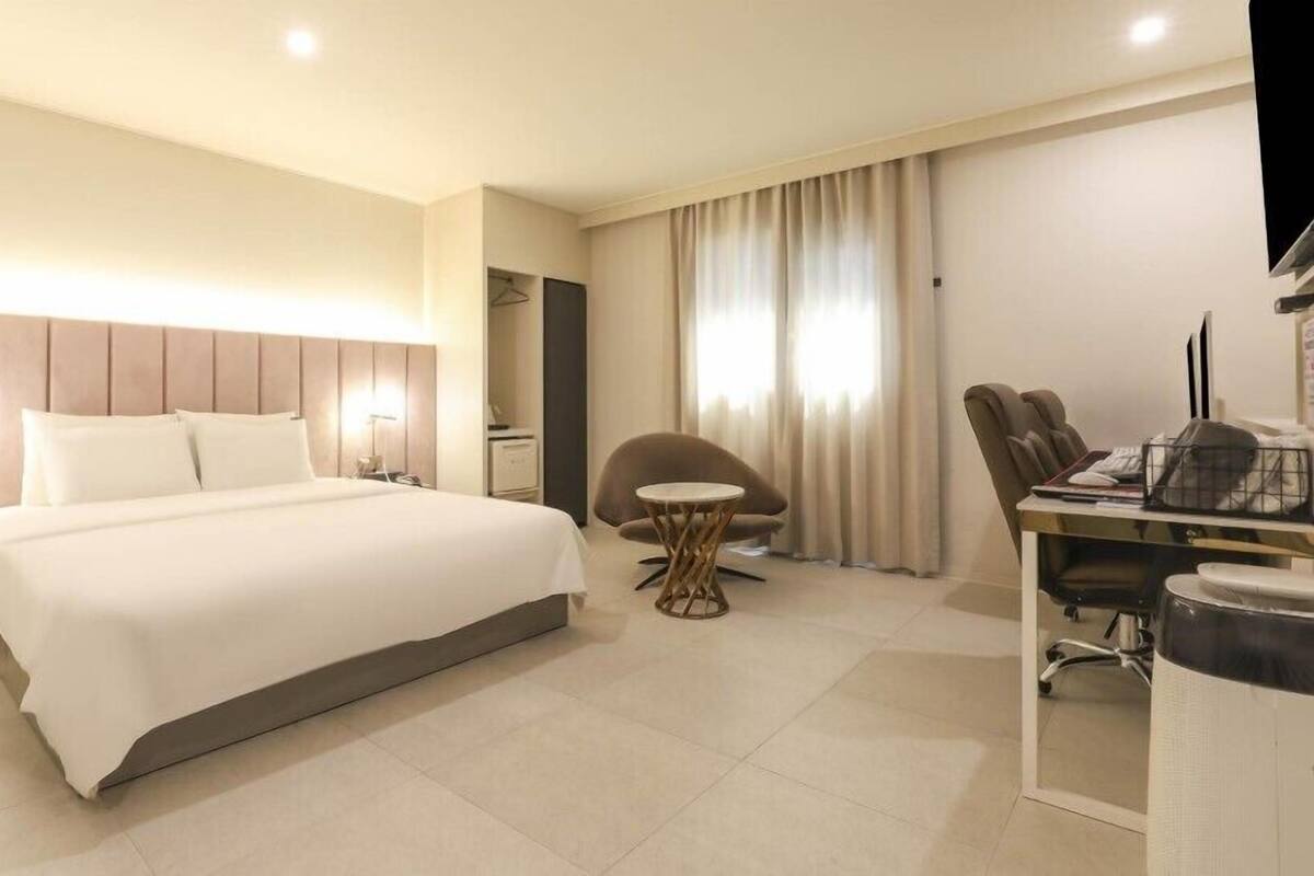 Una habitación de hotel con una cama grande, un escritorio con silla, una mesita redonda y un televisor.