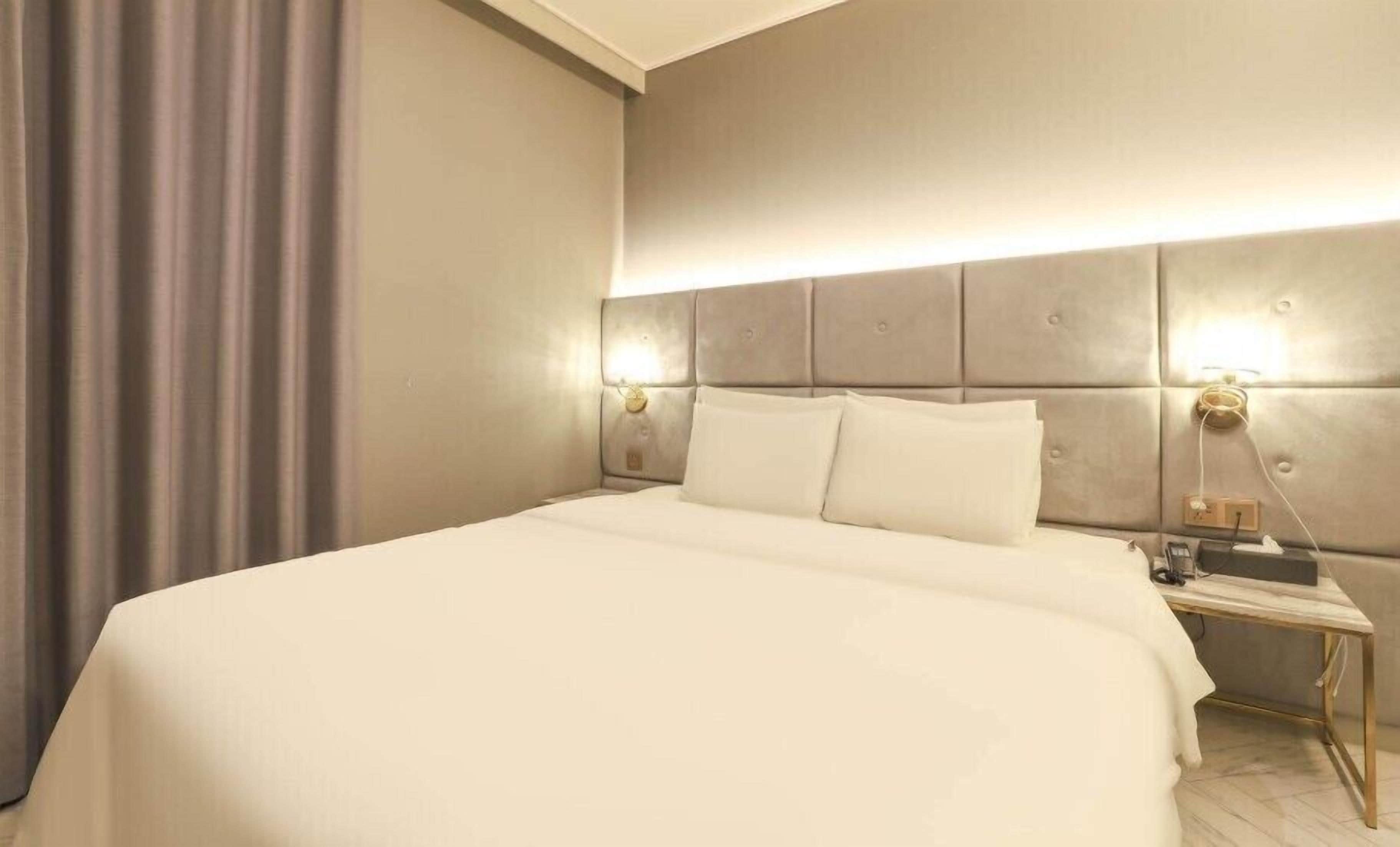 A hotel room with a large bed, a nightstand with a lamp, and a wall-mounted light fixture.