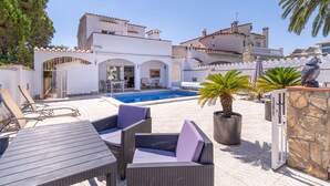 A poolside area with outdoor furniture, a stone wall, and a view of a building with multiple balconies.