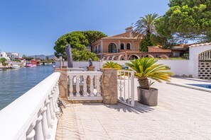 Una propiedad frente al mar con balaustrada de piedra, piscina y vista a barcos en el agua.