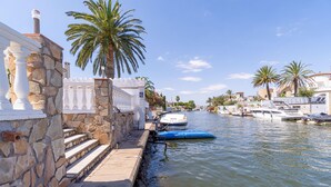 A stone waterfront with steps leading to a dock, palm trees, and boats.