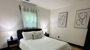 A modern bedroom with a large bed, two bedside tables with lamps, a ceiling light, and abstract wall art. - Marvelous 3-bedroom house with AC in Charlotte (Charlotte)