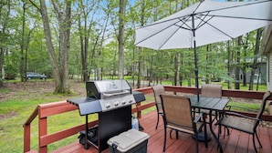 A deck with a grill, a table with chairs, and an umbrella.