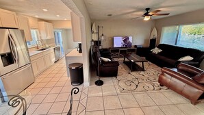 Una cocina moderna con refrigerador, estufa y lavaplatos. Hay un comedor con mesa y sillas, y una sala de estar con sofá y televisor.