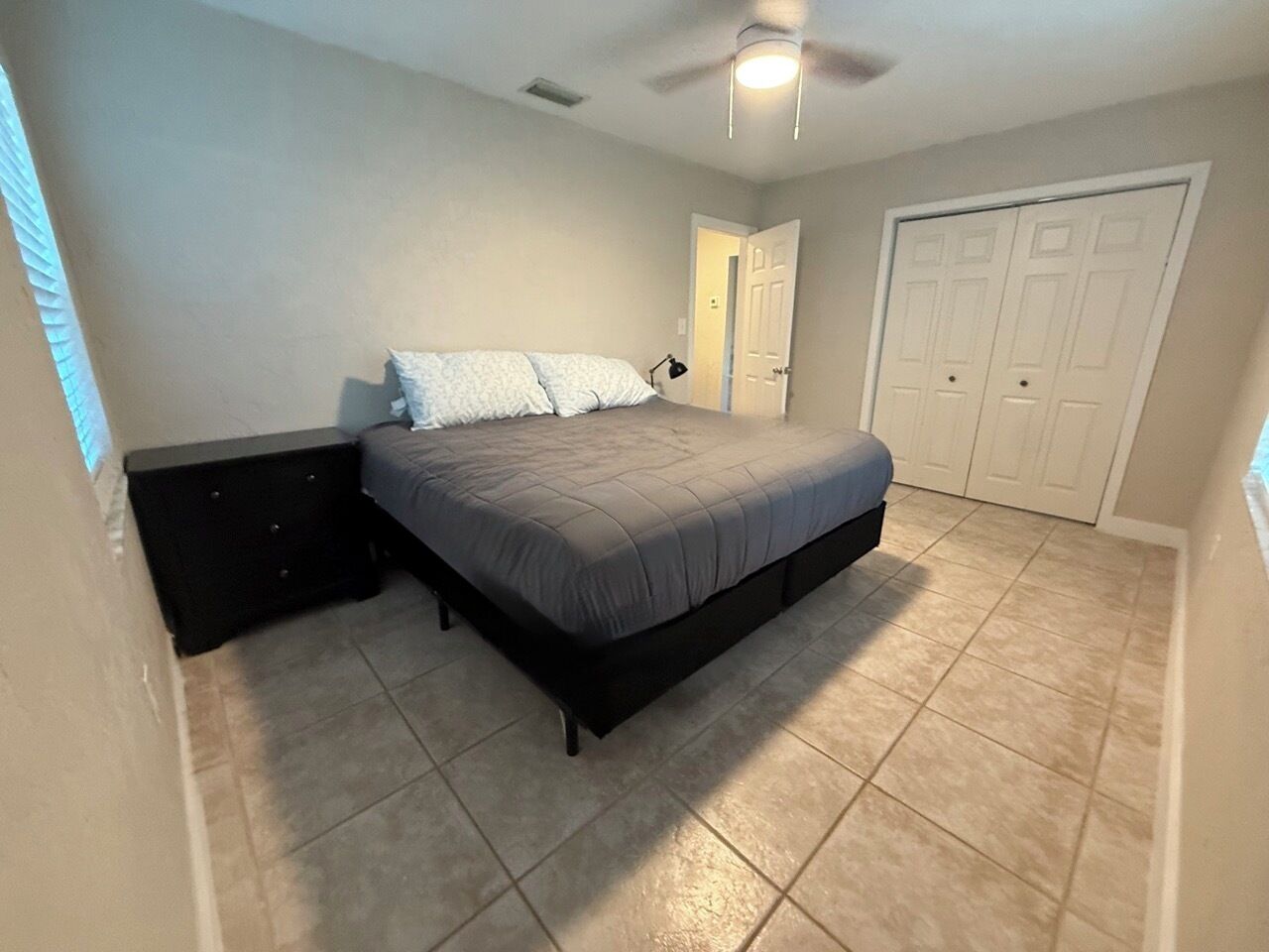 A bedroom with a bed, a nightstand, a ceiling fan, and a door.