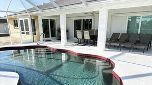 A swimming pool with clear water, surrounded by a covered patio with chairs and a table. - Sunny Pool Villa – Bikes, Beaches & Golf (Rotonda West)