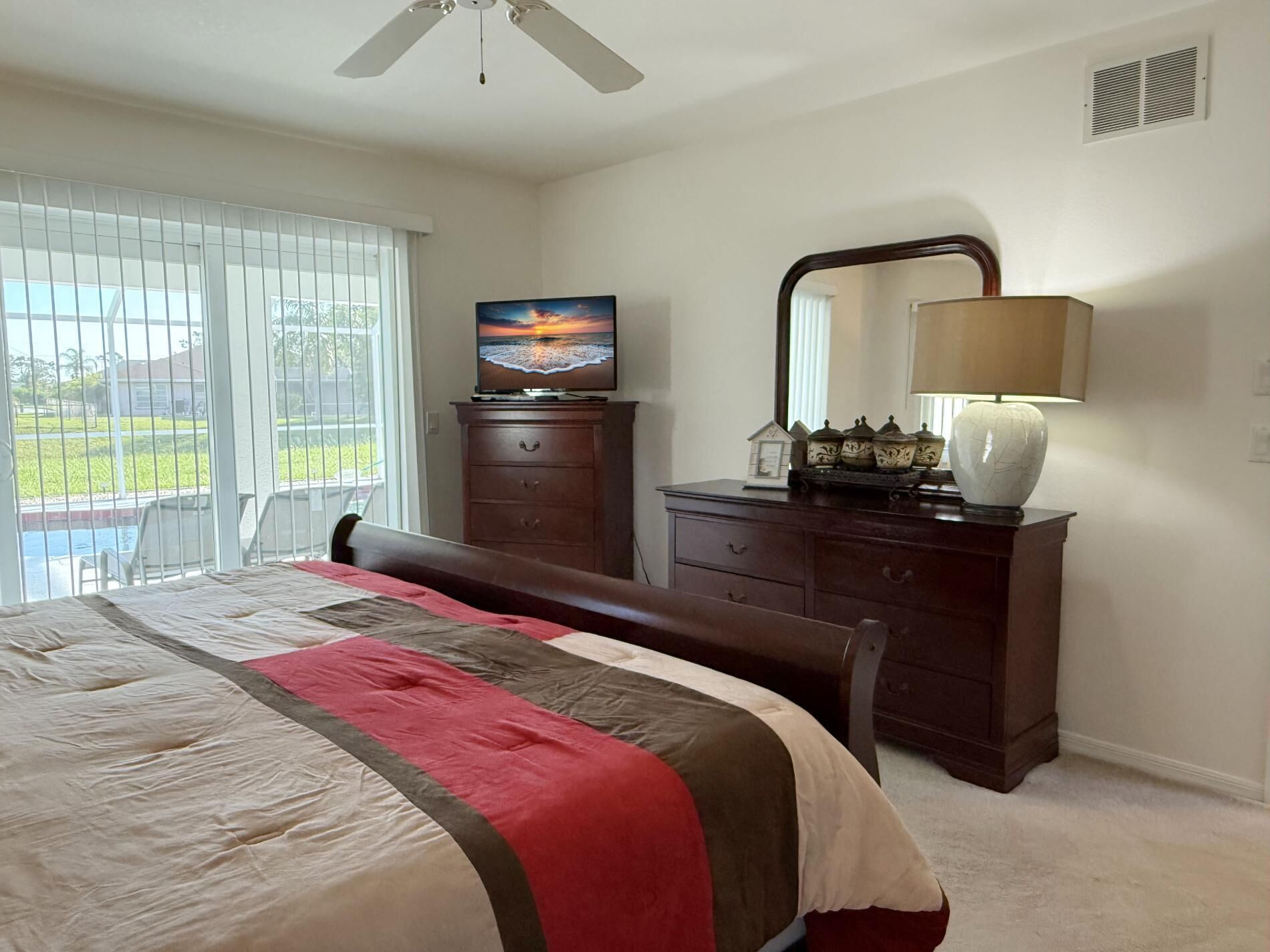 A bedroom with a bed, a dresser, a TV, and a lamp.