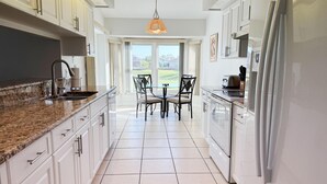 A modern kitchen with white cabinets, granite countertops, a built-in oven, and a dining area with a table and chairs. - Sunny Pool Villa – Bikes, Beaches & Golf (Rotonda West)