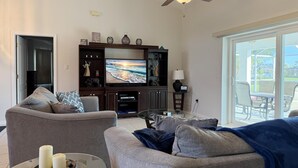 A living room with a flat-screen TV, dark wood entertainment unit, grey sofas, and a glass coffee table. - Sunny Pool Villa – Bikes, Beaches & Golf (Rotonda West)