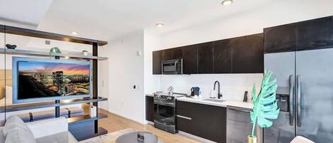 Een moderne woonkamer met een flatscreen televisie, een bank, een salontafel en een keuken met donkere kastjes, een magnetron en een koelkast.