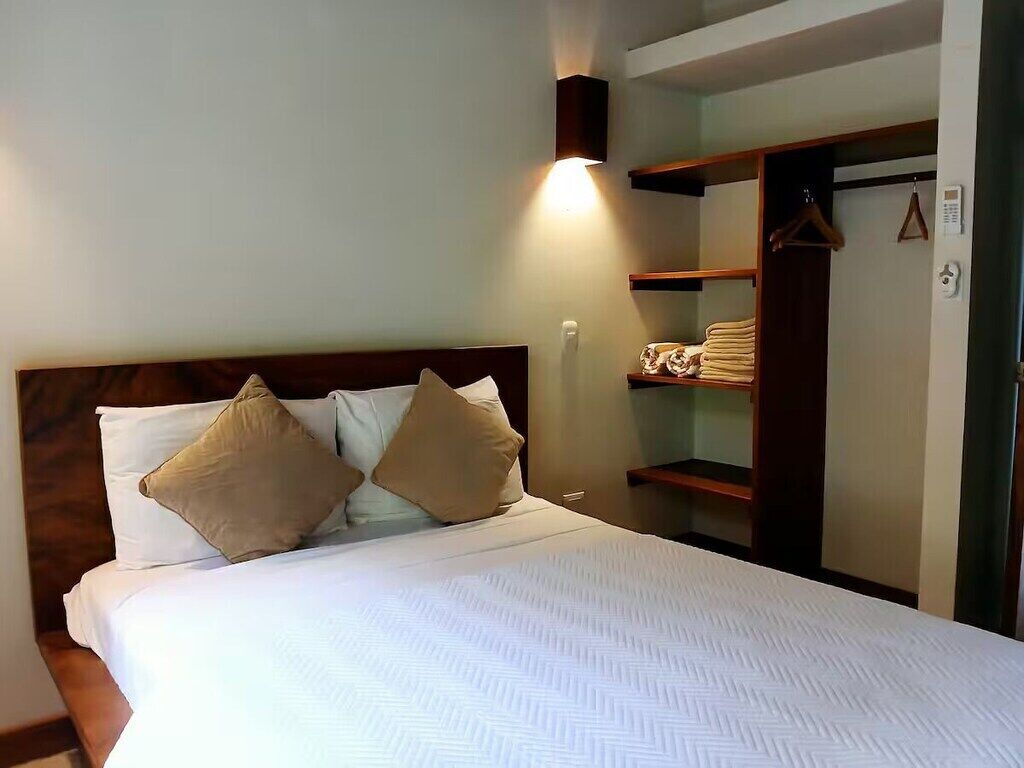 A neatly made bed with two pillows, a bedside table, and a wardrobe with hanging clothes.