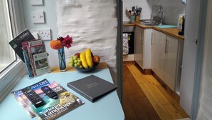 Una cocina con armarios de madera, una encimera y un cuenco de fruta. Hay revistas y un libro sobre la encimera.