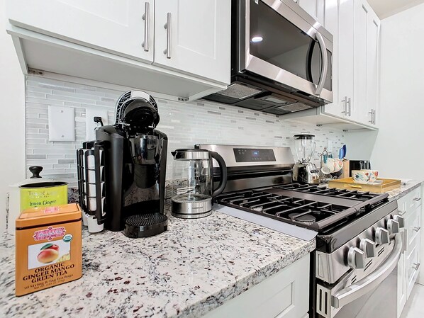 A kitchen with stainless steel appliances, a coffee maker, a blender, and a box of organic tea.
