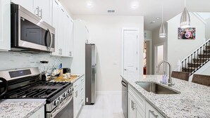 A modern kitchen with stainless steel appliances, white cabinetry, granite countertops, and pendant lighting. - 4 Bed Villa-Sleeps 8-Pool-Gym-15 min to Disney (Kissimmee)