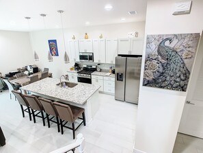 Una cocina moderna con armarios blancos, una isla central, electrodomésticos de acero inoxidable y un cuadro decorativo de un pavo real.