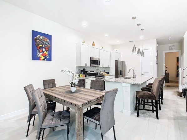 Cocina moderna con armarios blancos, electrodomésticos de acero inoxidable y una mesa de comedor de madera con sillas tapizadas.