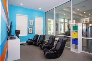 A room with blue walls, white blinds, exercise chairs, a desk with a computer, and a glass wall with a view of the outside.