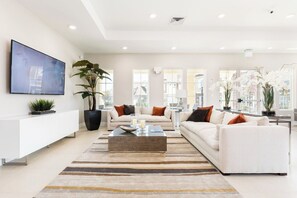 Una sala moderna con televisor de pantalla plana, una planta grande en maceta, un conjunto de sofás y una mesa de centro.