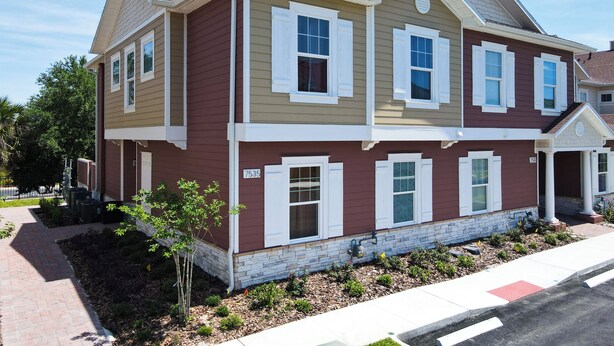 A two-story residential building with a stone foundation, a red and beige color scheme, and a brick pathway leading to the entrance. - 4 Bed Villa-Sleeps 8-Pool-Gym-15 min to Disney (Kissimmee)