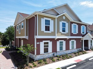 A two-story residential building with a stone foundation, a red and beige color scheme, and a brick pathway leading to the entrance.