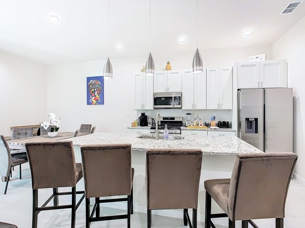 A modern kitchen with white cabinets, a central island with seating, stainless steel appliances, and pendant lighting.