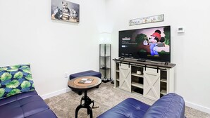 A living room with a flat-screen TV, blue sofas, a small table, and a decorative wall piece. - 4 Bed Villa-Sleeps 8-Pool-Gym-15 min to Disney (Kissimmee)