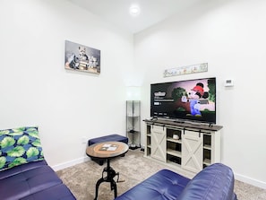 Un soggiorno con televisione a schermo piatto, divani blu, un tavolino e un elemento decorativo a parete.
