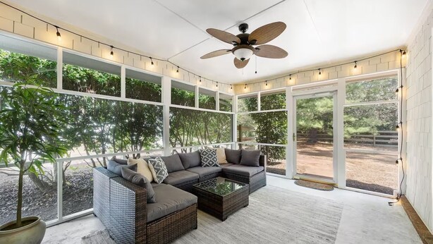 A spacious sunroom with a sectional sofa, large windows, and a ceiling fan.
