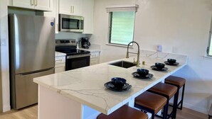 A modern kitchen with white cabinets, stainless steel appliances, a marble countertop, and bar stools. - Ocean view A/C, pool/hot tub coconut marketplace (Kapaʻa)