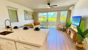 A modern kitchen with a large island, a dining area with a table and chairs, and a balcony with a view of the outdoors. - Ocean view A/C, pool/hot tub coconut marketplace (Kapaʻa)