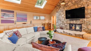 Una sala de estar acogedora con chimenea de piedra, un televisor de pantalla plana grande y un techo de madera con tragaluces.