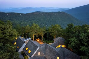 A mountain lodge with multiple roofs, surrounded by dense forest and distant mountain ranges.