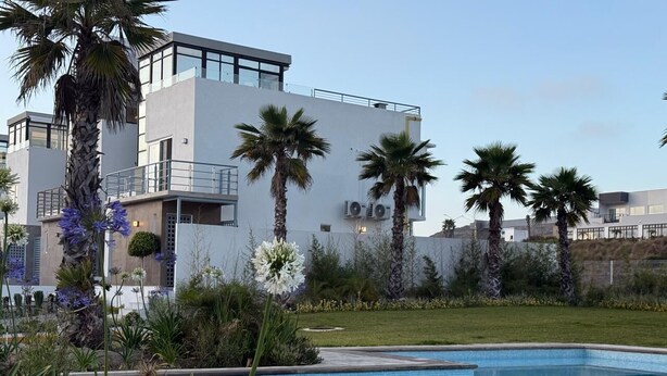 A modern building with a swimming pool, surrounded by palm trees and various plants.