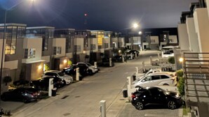 A nighttime view of a residential street with modern buildings, parked cars, and streetlights.