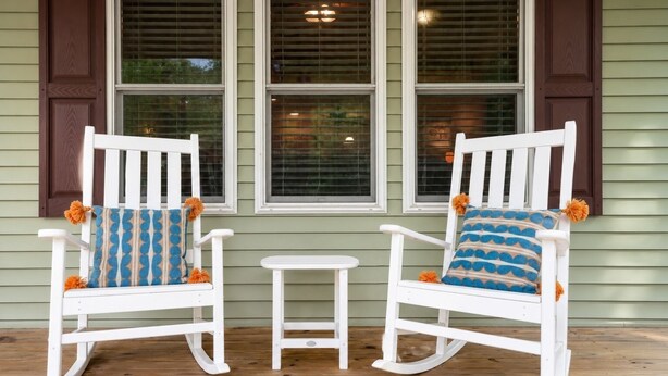 Two rocking chairs with patterned cushions and orange pom-poms, positioned on a wooden deck in front of a house with green siding and brown shutters. - Serenity Cottage Deck, Game Room & Fire Pit near Narrowsburg Masthope (Lackawaxen)
