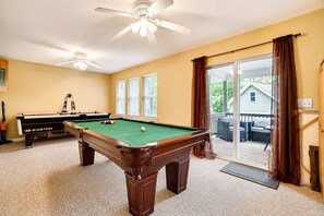A pool table in a room with a ceiling fan, a window with blinds, and a view of a house through a sliding glass door. - Serenity Cottage Deck, Game Room & Fire Pit near Narrowsburg Masthope (Lackawaxen)