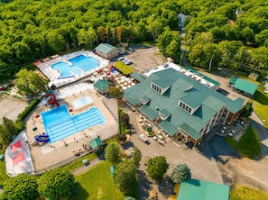 Vista aérea de un complejo turístico con una gran piscina, un área de piscina separada y un edificio con techo verde.