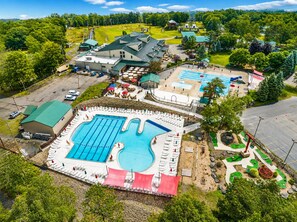 Vue aérienne d’un complexe hôtelier doté d’une grande piscine, de plusieurs bâtiments et d’un environnement verdoyant.