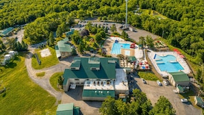 An aerial view of a resort with multiple swimming pools, a large building with a green roof, and surrounding forested areas. - Serenity Cottage Deck, Game Room & Fire Pit near Narrowsburg Masthope (Lackawaxen)