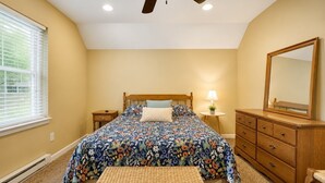 A bedroom with a bed, a dresser, a mirror, a ceiling fan, and a window with blinds. - Serenity Cottage Deck, Game Room & Fire Pit near Narrowsburg Masthope (Lackawaxen)