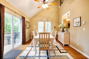 A dining area with a large table, chairs, a ceiling fan, and a view of the outdoors through a sliding glass door.