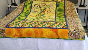 A bed with a colorful quilt, a brown headboard, and two bedside lamps. - Sweet Rushmore Suite (Rapid City)