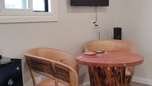 A room with two wicker chairs, a round wooden table, a flat-screen TV mounted on the wall, and a black speaker on the floor. - Sweet Rushmore Suite (Rapid City)