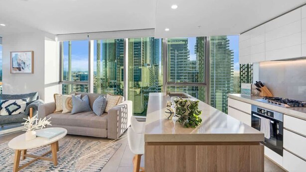 A modern apartment with a kitchen, living area, and large windows offering city views. - NEW Ocean view 1BR | Pool, Parking & Walk to Beach (Broadbeach)